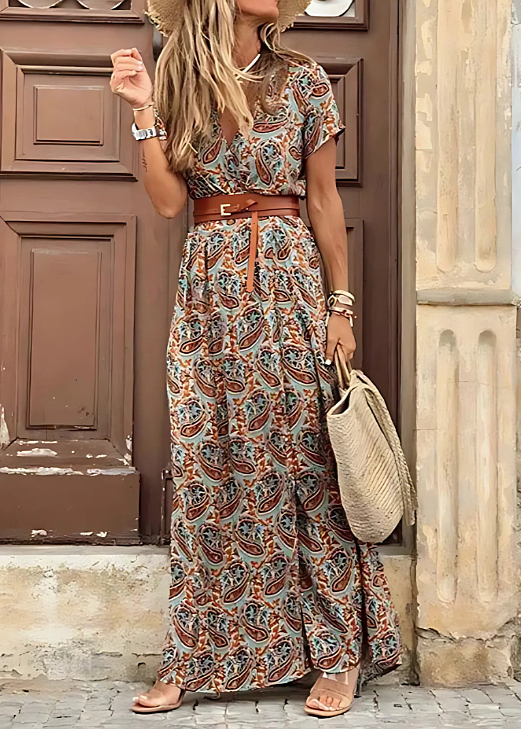 Women's earth-toned paisley floral print short sleeve maxi dress with a brown belt, standing in front of a wooden door.