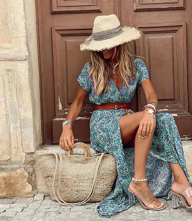 Women's blue and green paisley floral print short sleeve maxi dress with a brown belt, seated, wearing a straw hat.