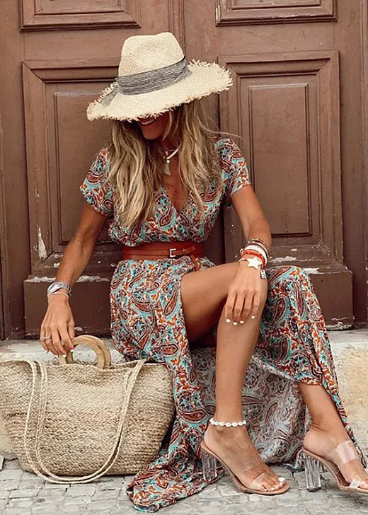 Women's rust and teal paisley floral print short sleeve maxi dress with a brown belt, seated, wearing a straw hat.