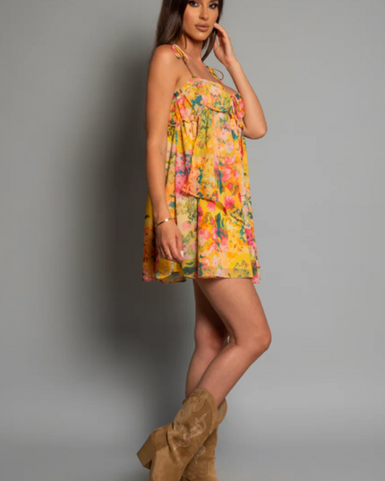 Side profile of a women's yellow floral print tie shoulder mini dress, styled with tan cowboy boots.