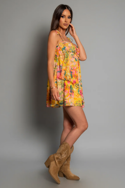 Side profile of a women's yellow floral print tie shoulder mini dress, styled with tan cowboy boots.