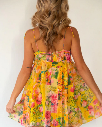 Back view of a women's yellow floral print tie shoulder mini dress, showing the ruffled hem.
