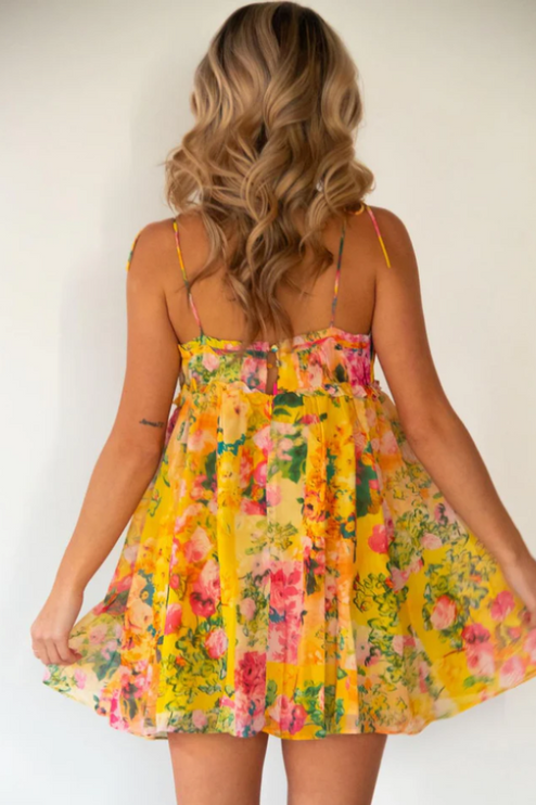 Back view of a women's yellow floral print tie shoulder mini dress, showing the ruffled hem.