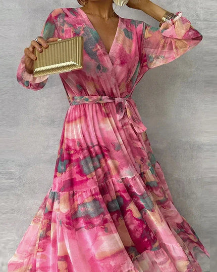 Full-length view of a women's pink floral long sleeve maxi dress with a V-neck and ruffled cuffs, holding a clutch.