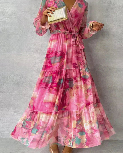 Women's pink floral printed V-neck long sleeve maxi dress with tiered skirt and tie waist, holding a gold clutch.