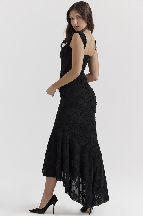 Side profile of a black floral ruched off-shoulder maxi dress, featuring a high-low hem and fitted silhouette with delicate floral texture.