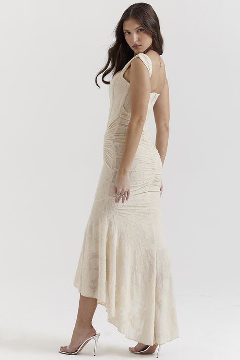 Side profile of a women's cream floral ruched maxi dress, featuring a high-low hem and subtle train.