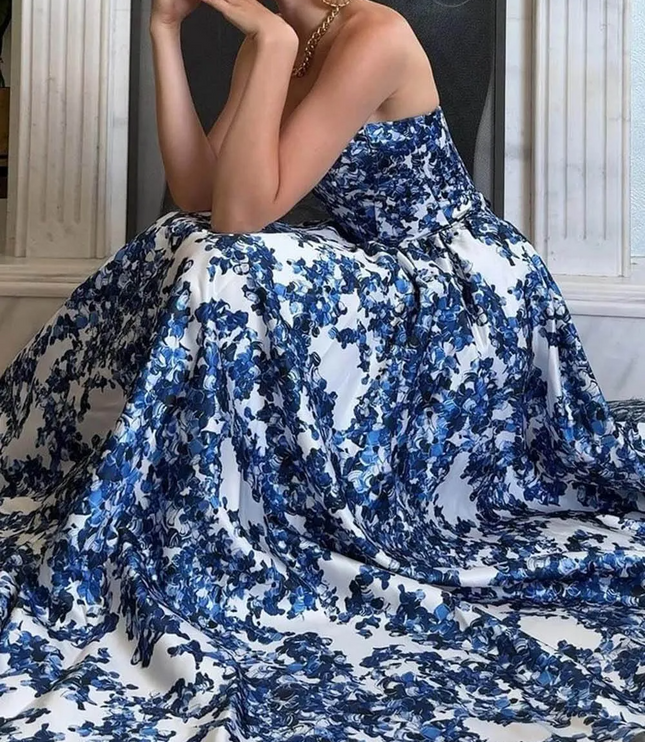 Seated view of a women's blue and white floral strapless formal maxi dress, showing the expansive skirt fabric and intricate pattern.
