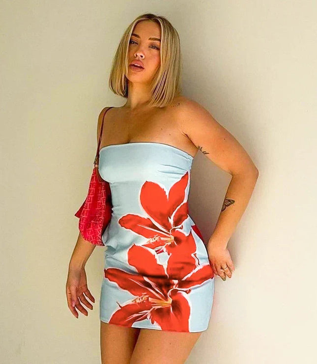 Blonde woman wearing a light blue strapless mini dress with bold red floral pattern, holding a pink bag.