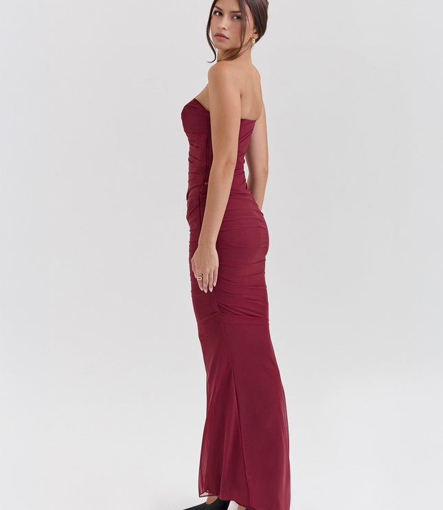 Side profile of a woman in a fitted deep red strapless ruched maxi dress with a sheer overlay, paired with black heels.