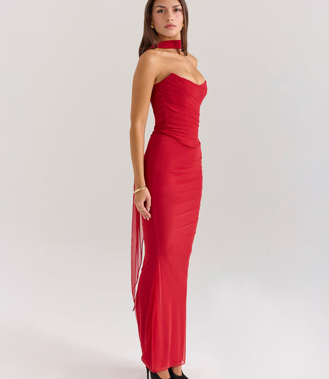 Side profile of red strapless ruched maxi dress with long flowing sheer panel, black heels.