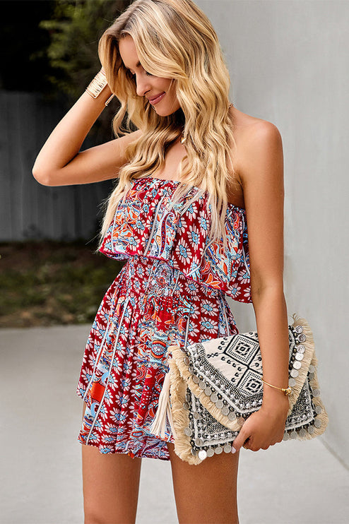 Women's red floral strapless ruffle mini romper with a smocked waist, holding a decorative clutch with tassels.