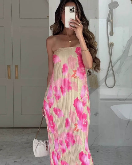 Women's pleated maxi dress with strapless design and vibrant pink floral pattern on a light background, paired with a white handbag.