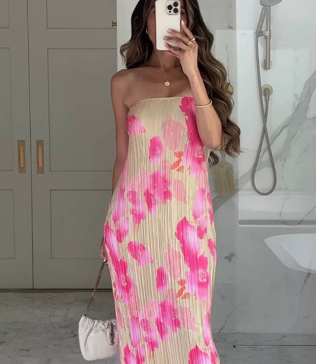 Women's pleated maxi dress with strapless design and vibrant pink floral pattern on a light background, paired with a white handbag.