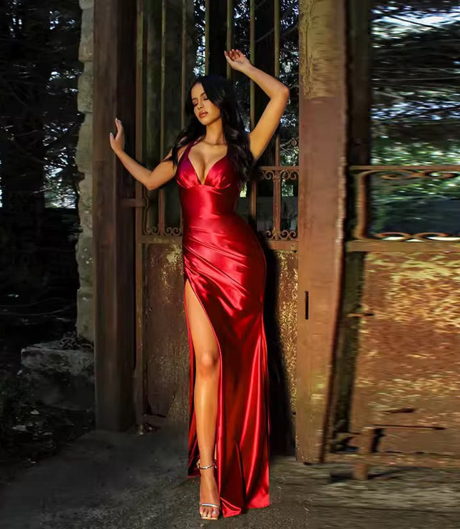 Full length view of a woman in a red formal backless V-neck slit maxi dress, posing by an old gate.