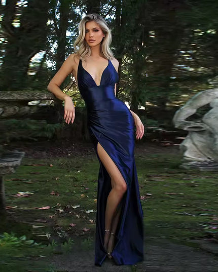 Navy blue formal backless V-neck maxi dress with a high slit, satin- fabric, in a garden setting.