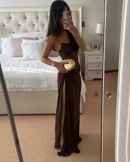 Side view of a woman in a brown off-shoulder lace corset maxi dress with a thigh-high slit, holding a gold clutch.
