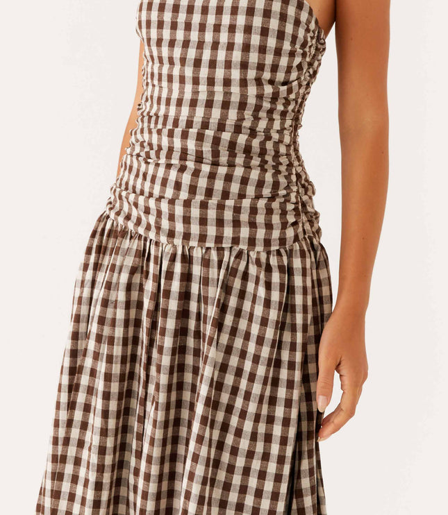 Close-up of the ruched bodice and flowing skirt on a brown and white gingham strapless maxi dress