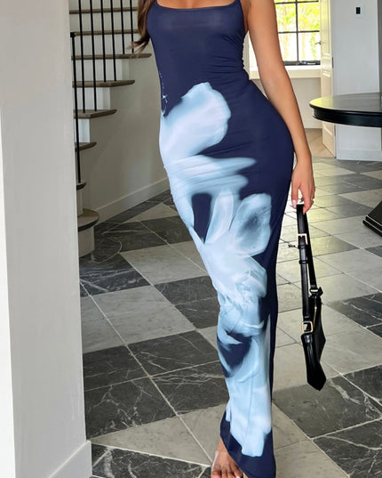 Women's greyscale floral low neck maxi dress with adjustable straps, dark navy with large white floral print, styled with clear heels and a black handbag.