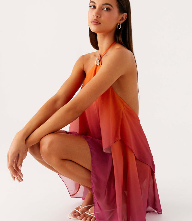 Women's ombre layered chiffon mini dress in orange and pink, posed in a crouching position to show the movement of the fabric.