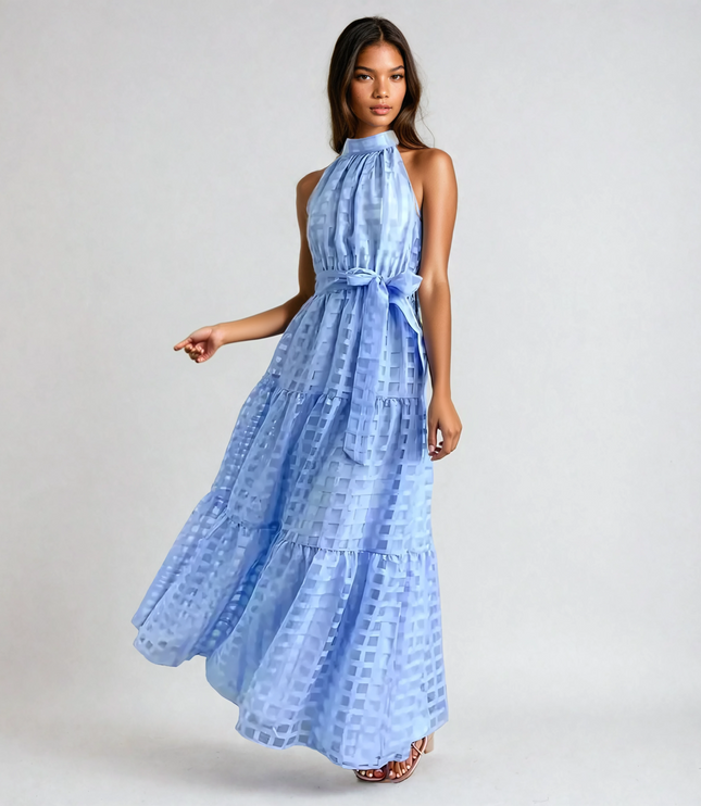 Dark-haired woman wearing a light blue halter neck tiered maxi dress with a subtle checkered pattern and waist tie.