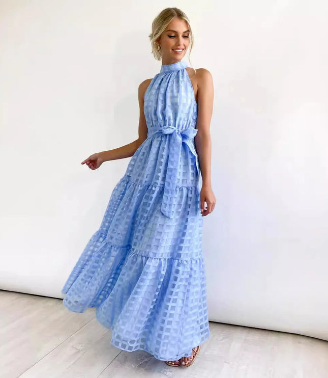 Smiling woman in a light blue halter neck tiered maxi dress, featuring a delicate checkered pattern and waist tie.