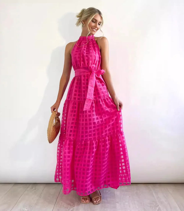 Vibrant pink halter neck tiered maxi dress, showcasing a checkered pattern, waist tie, and a woven bag.