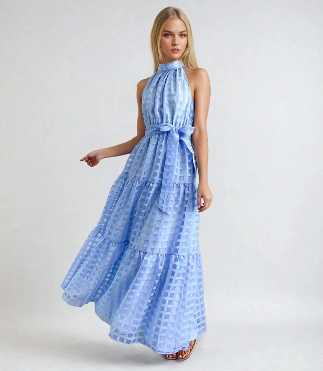 Blonde woman wearing a light blue halter neck tiered maxi dress with a delicate checkered pattern and waist tie.