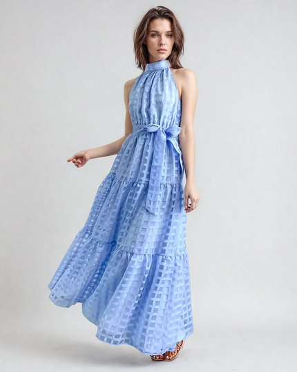 Woman with short brown hair in a light blue halter neck tiered maxi dress, featuring a checkered pattern and waist tie.