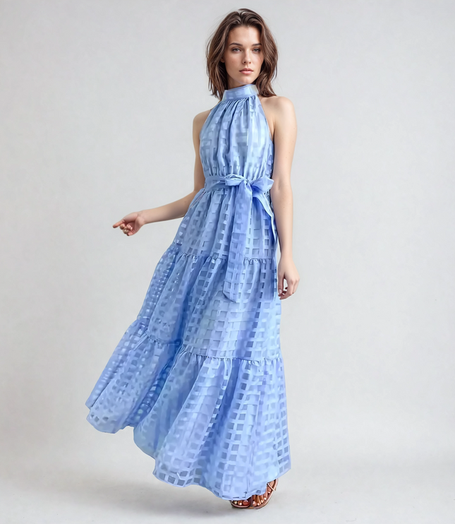 Woman with short brown hair in a light blue halter neck tiered maxi dress, featuring a checkered pattern and waist tie.