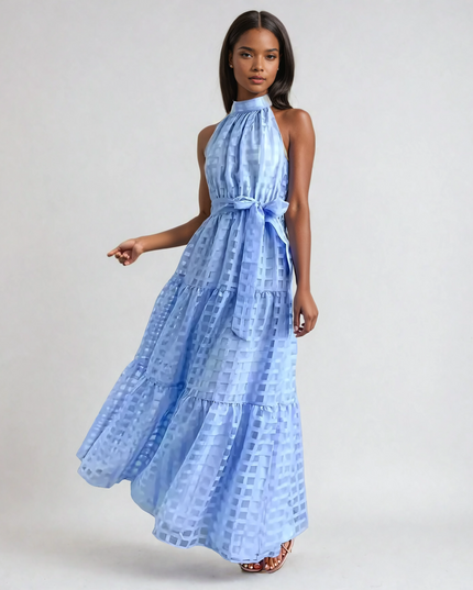 Light blue halter neck tiered maxi dress with a subtle checkered pattern and waist tie, flowing elegantly.