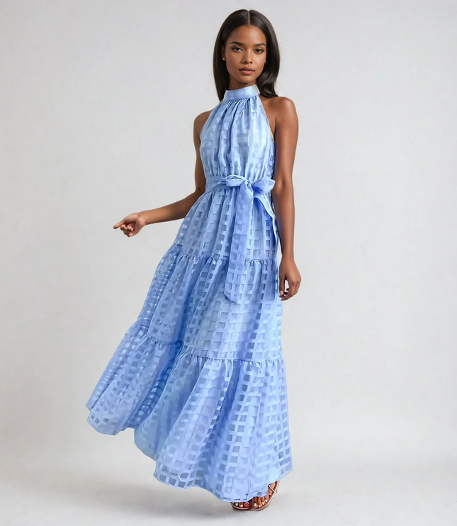 Light blue halter neck tiered maxi dress with a subtle checkered pattern and waist tie, flowing elegantly.