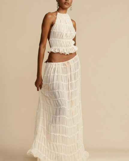 Front view of the women's ivory halter ruffle trim crop top and maxi skirt set, with the model holding the skirt fabric.
