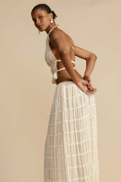 Side profile of the women's ivory halter ruffle trim crop top and maxi skirt set, highlighting the flow of the skirt.