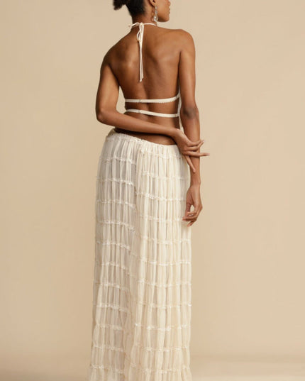 Back view of the women's ivory halter ruffle trim crop top and maxi skirt set, with hands crossed behind the back.
