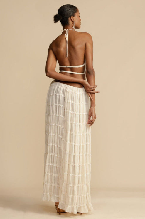 Back view of the women's ivory halter ruffle trim crop top and maxi skirt set, with hands crossed behind the back.