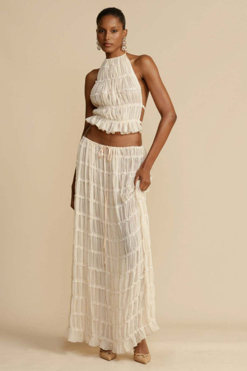 Full-length view of a women's ivory halter ruffle trim crop top and matching maxi skirt set, featuring delicate ruffles and a drawstring waist.