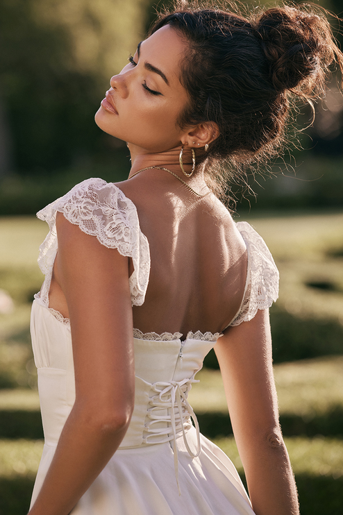 Back view of a white women's mini dress featuring delicate lace cap sleeves and a corset-style lace-up back closure.