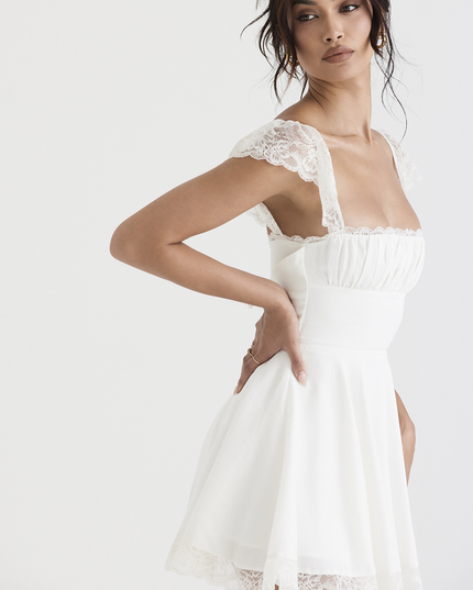 Side profile of a white women's mini dress, showing the elegant lace cap sleeves, square neckline, and structured waistline.