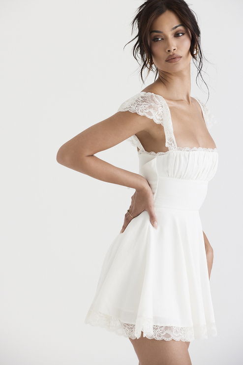 Side profile of a white women's mini dress, showing the elegant lace cap sleeves, square neckline, and structured waistline.