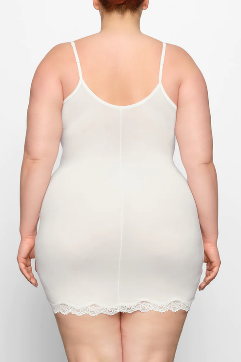 Back view of a plus-size woman in the ivory lace trim scoop neck mini slip dress, showing the full coverage and lace hem.
