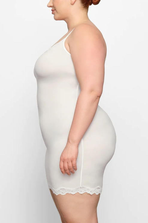 Side profile of a plus-size woman in the ivory lace trim scoop neck mini slip dress, showcasing the garment's drape.