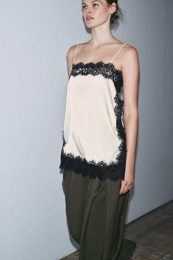 Side view of a women's cream satin camisole mini dress featuring black lace details and delicate straps.
