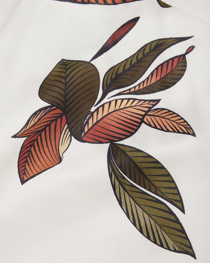 Detailed close-up of the vibrant green and orange leaf print pattern on the white midi wrap dress material.