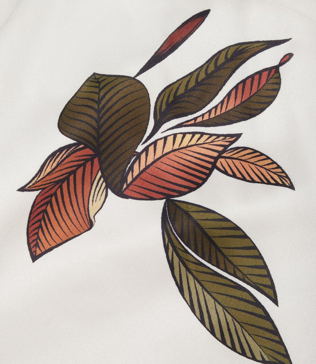 Detailed close-up of the vibrant green and orange leaf print pattern on the white midi wrap dress material.