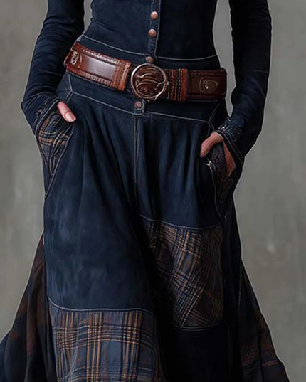 Detailed view of the plaid panel on the dark blue maxi dress, with a brown belt and hands in pockets.