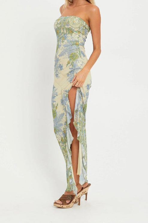 Side profile of a women's bandeau maxi dress, showcasing the intricate blue and green paisley print and ruffled high slit detail.