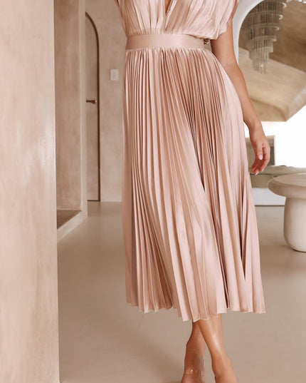 Side profile of a women's light pink pleated v-neck midi dress, highlighting the graceful flow of the skirt.