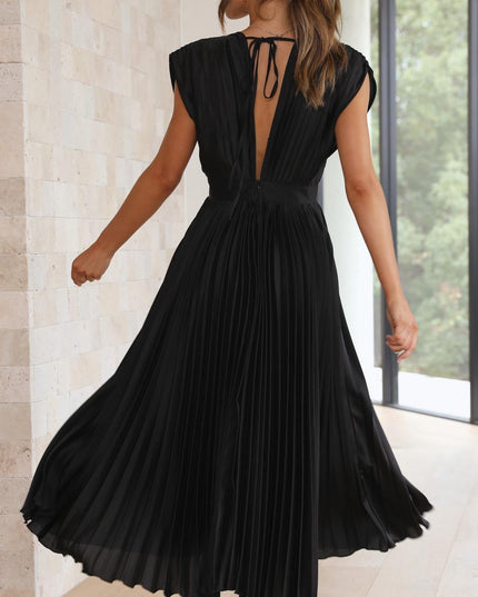 Back view of the black pleated v-neck midi dress, capturing the deep V-back and the movement of the pleated skirt as the model turns.