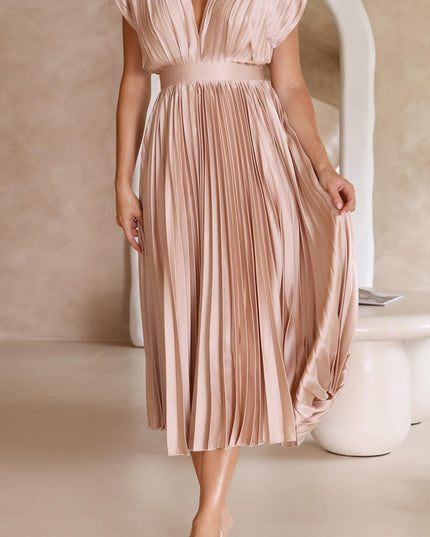 Front view of a women's light pink pleated v-neck midi dress, with a wide waistband and flowing skirt, paired with clear heels.